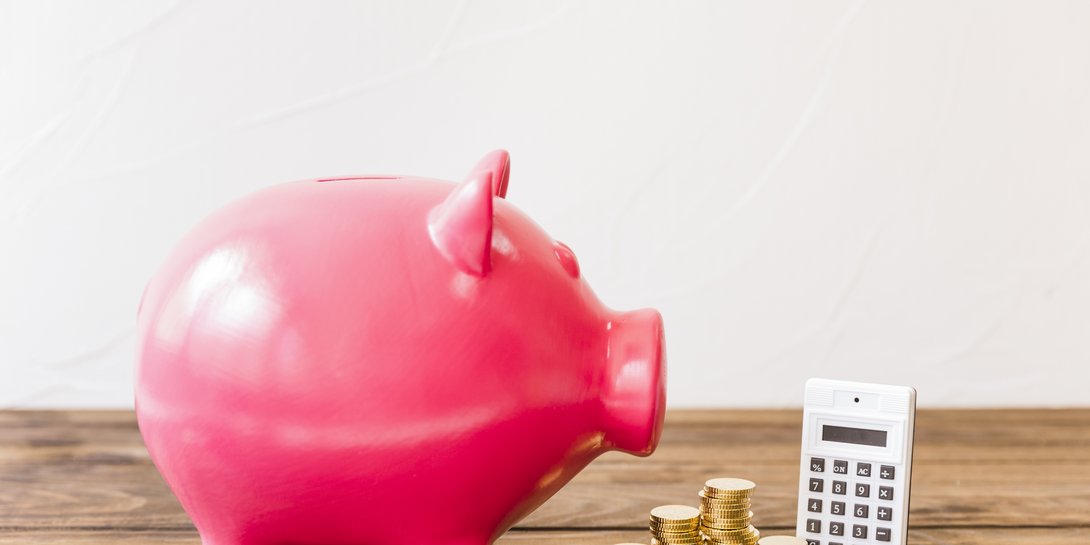 pink-piggybank-besides-calculator-stacked-coins-wooden-surface.jpg