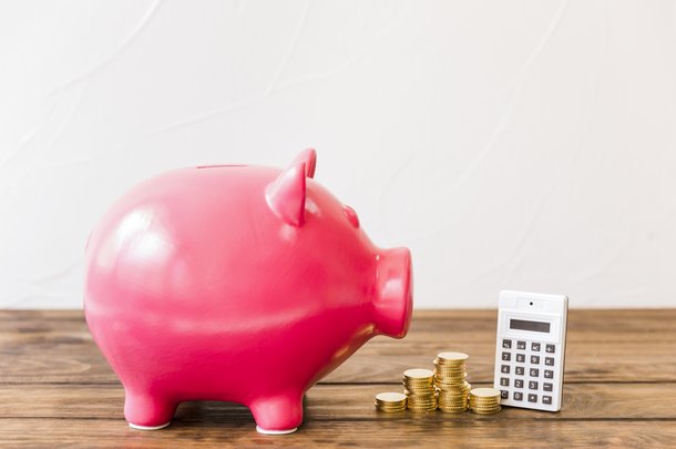 pink-piggybank-besides-calculator-stacked-coins-wooden-surface.jpg